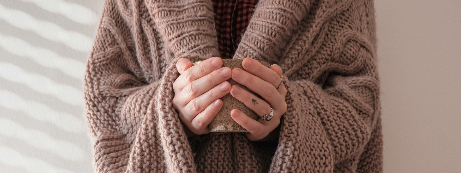 Eponyms in English: a woman wears a brown cardigan while holding a mug. Cardigan is an eponym in English.
