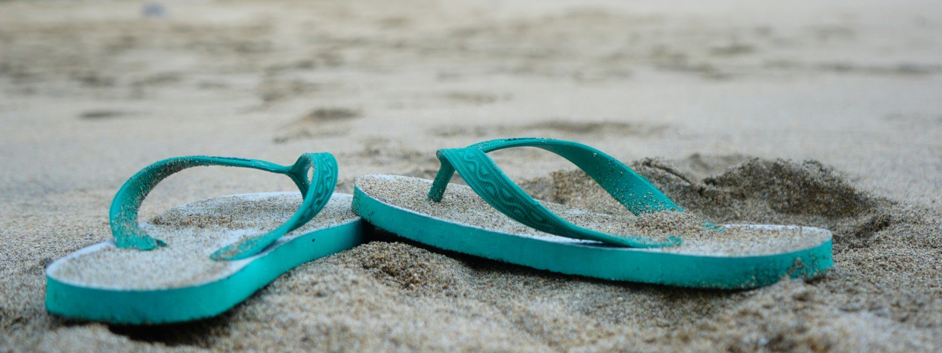 Ablaut Reduplication: a pair of blue flip flops sit in the sand on the beach.
