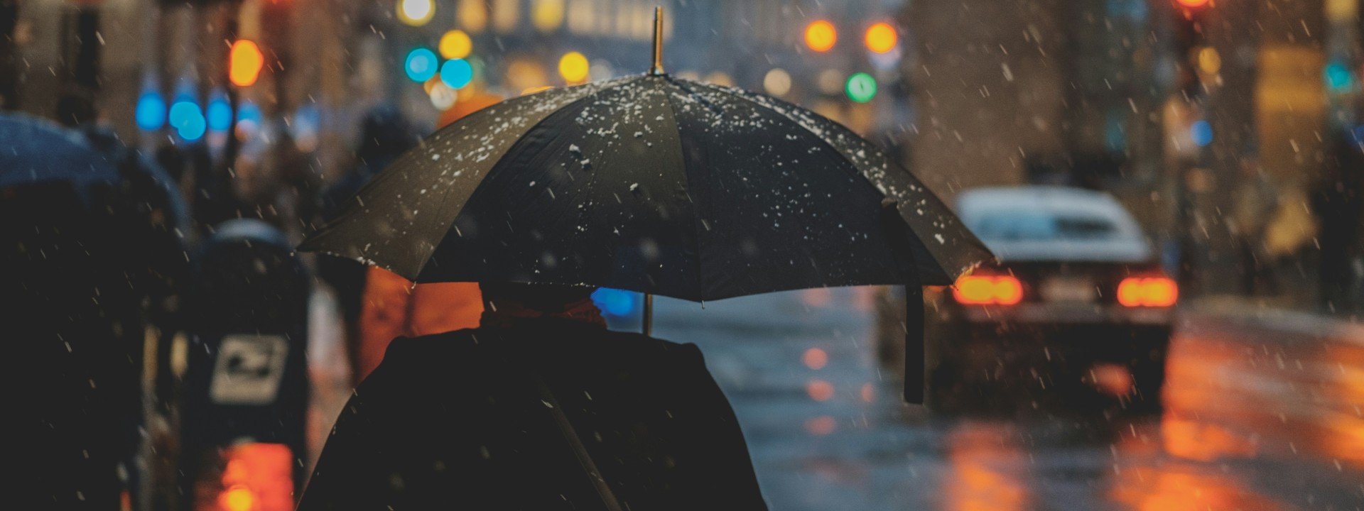 Rainy day vocabulary in English: a man walks through a city at night with an umbrella in the rain.