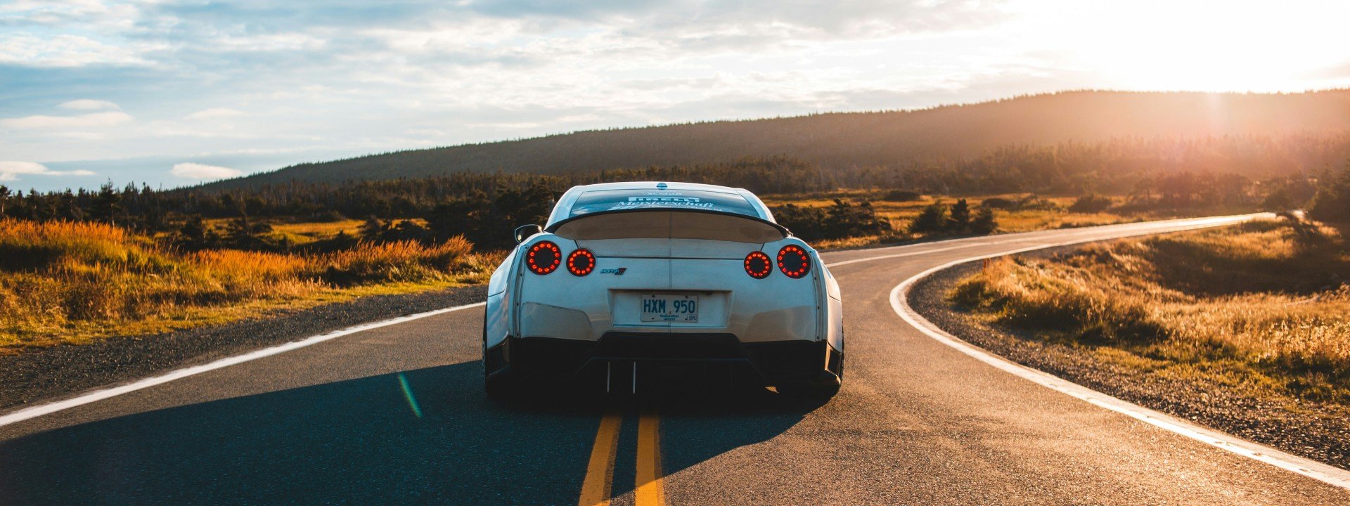 How to Rent a Car in English: A silver car drives around a curve at sunset.
